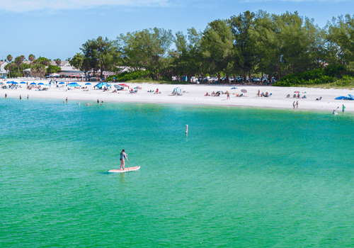 manatee beach on an afternoon day with turquoise water and blue sky and a person on a paddleboard