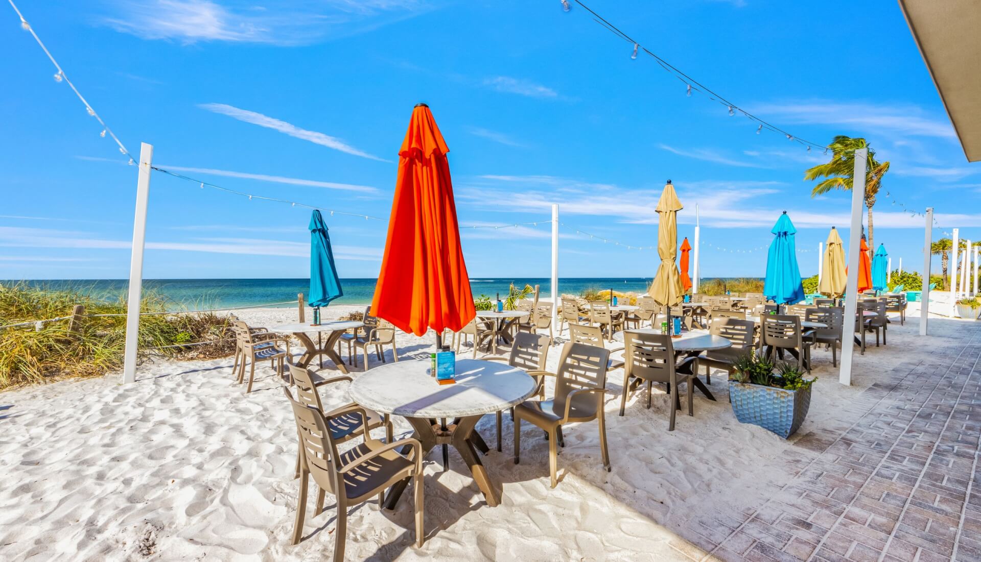 day exterior of beach house watefront restaurant with bright umbrellas and tables in the sand
