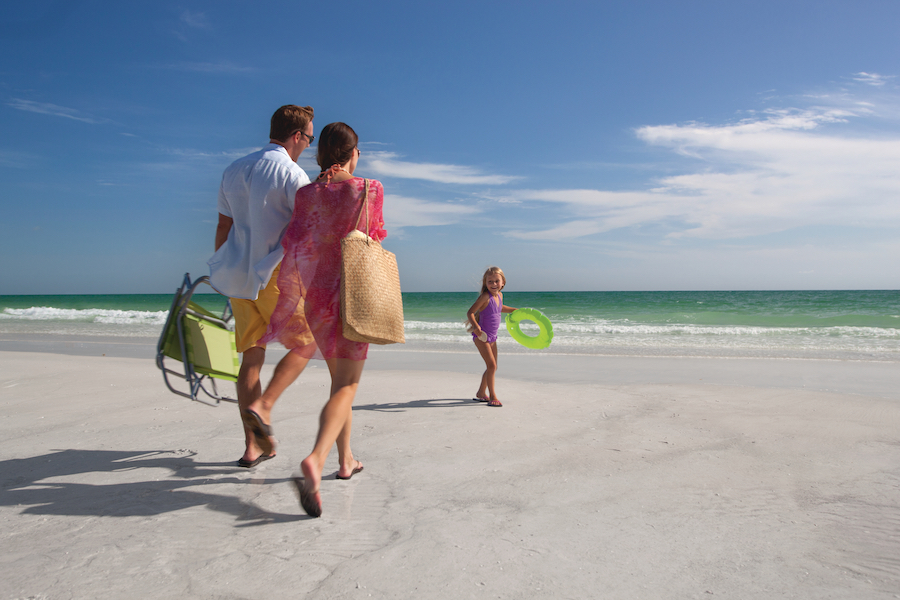 Request For Proposal - Convention Center Two parents hold hands as they walk towards the breaking waves at a beach in Bradenton, Florida, led by a girl holding a green frisbee who smiles at them.