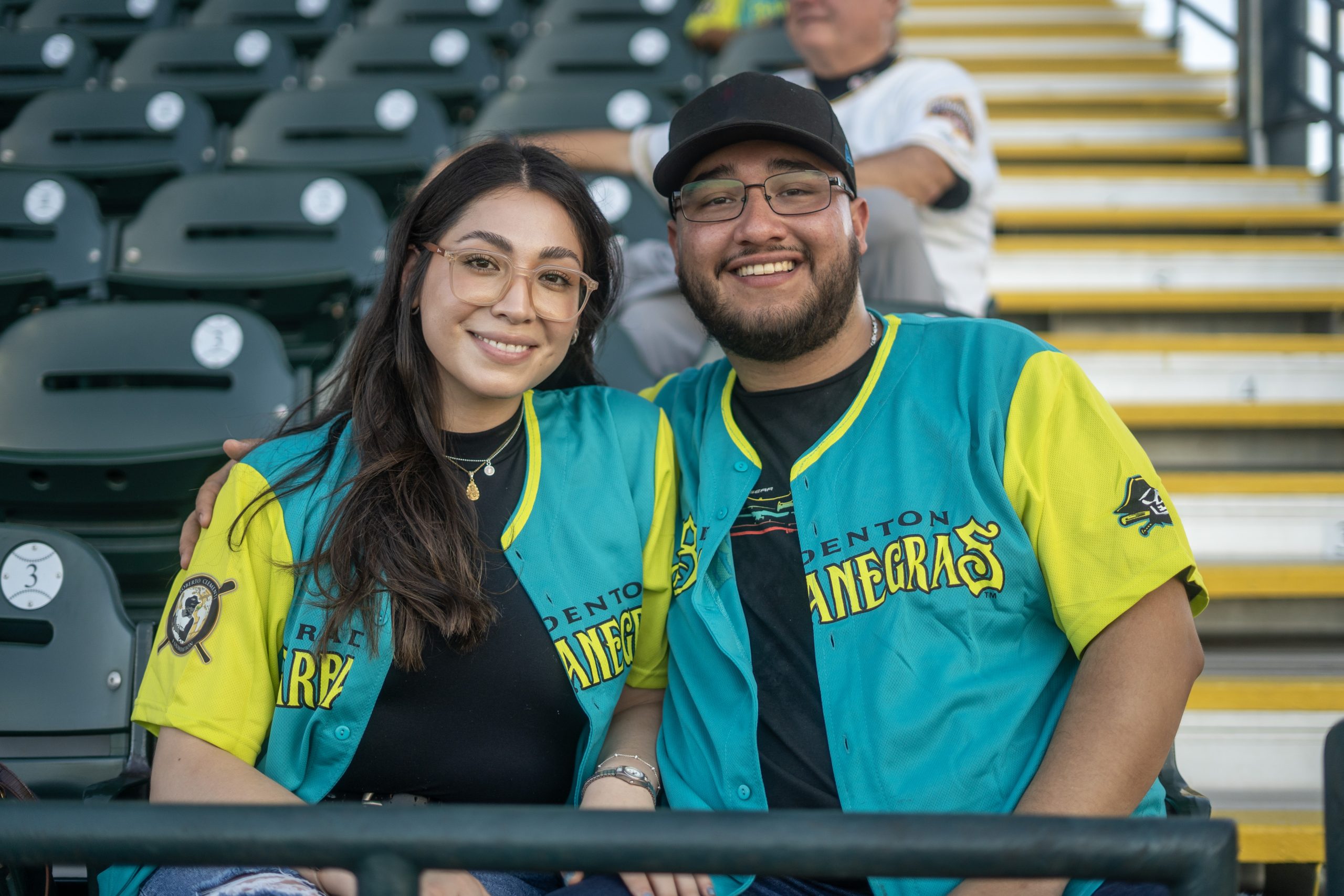 Hispanic couple in stands wearing teal & lime jerseys