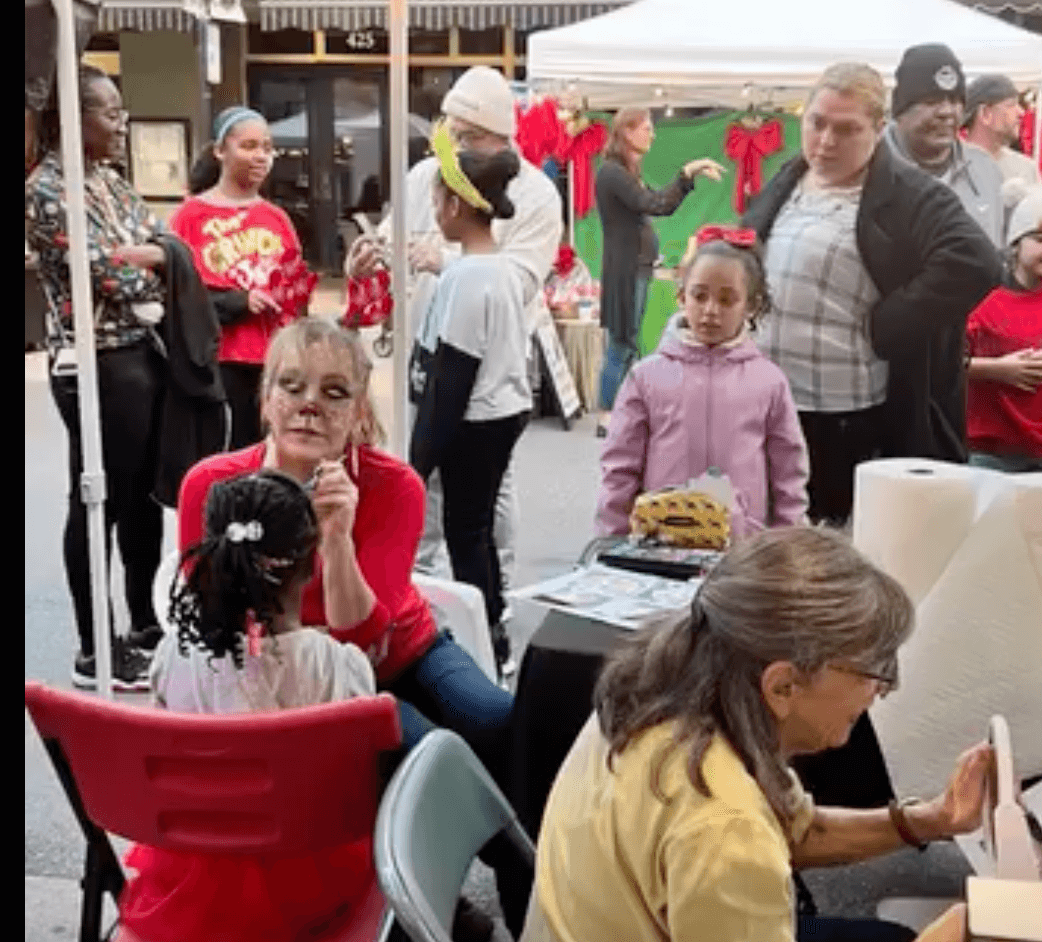 Picture of artist face painting a child with a crowd watching in line.