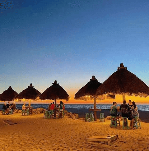 small tiki hut covered tables at dusk at Gulf Drive Cafe in the sand