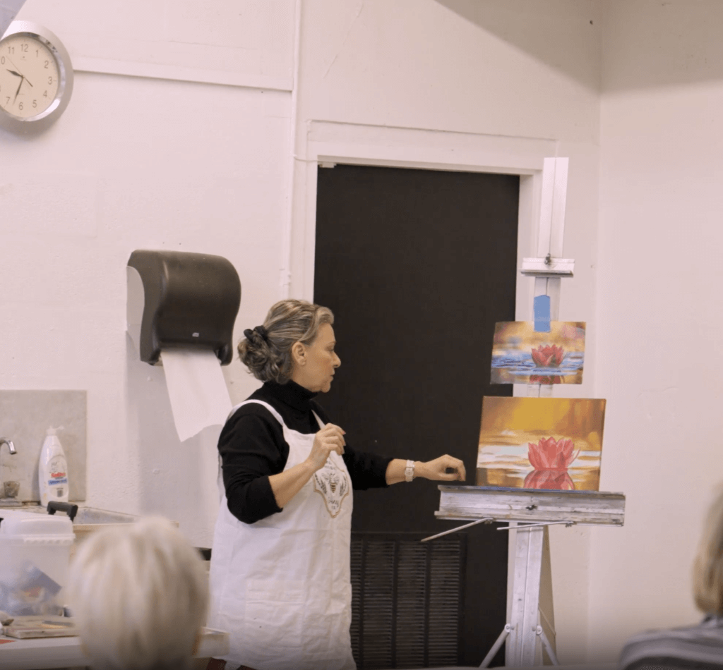 woman with two canvases teaching an art class